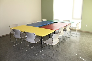 A room with multiple colorful tables and chairs arranged for group activities.
