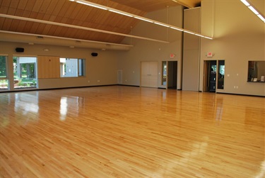 A spacious, empty room with a polished wooden floor and a high ceiling with wood paneling and modern lighting.