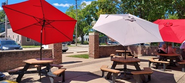 Two red umbrellas and one light gray umbrella shade picnic tables outside on a sunny day.