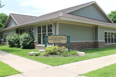 A pale green building with a brown roof, identified by a wooden sign as the South Side Neighborhood Center at 1300 South Sixth.