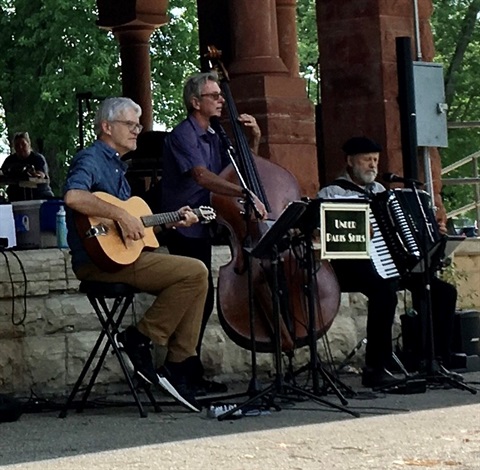 3 members of the band Under Paris Skies. one member playing guitar, one member playing bass, and on member playing accordion. 