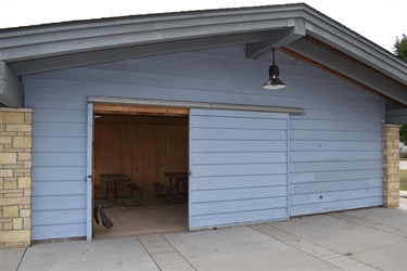 A light blue building with a large sliding door, revealing picnic tables inside.