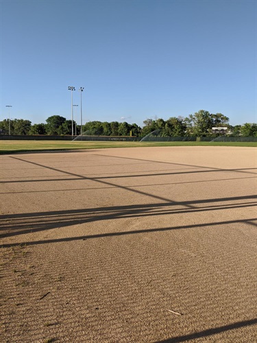 A baseball field with sprinklers watering the outfield under a clear blue sky.