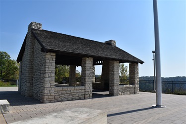 Stone pavilion with a dark roof and stone chimneys against a clear blue sky.