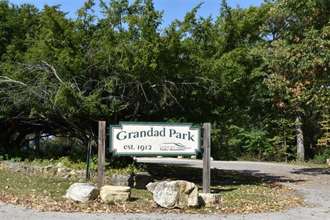 A sign for Grandad Park, established in 1912, stands near a tree-lined entrance.