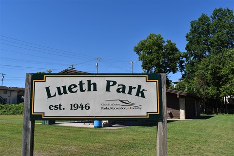 Lueth Park sign est. 1946 with City of La Crosse Parks Recreation & Forestry logo next to a park building on a sunny day.