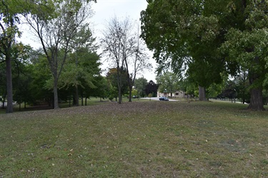 A grassy park with scattered trees and a house in the background.