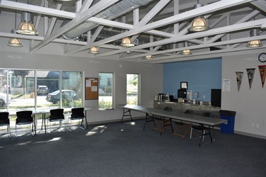 An empty community room with tables, chairs, a coffee station, and pennants on the wall.