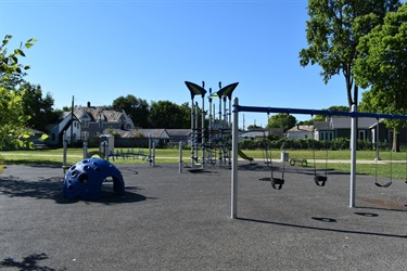A modern playground with swings, a climbing dome, and a jungle gym on a black rubber surface under a clear blue sky.