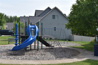 A blue plastic slide and swingset are featured in a playground with a gray house in the background.
