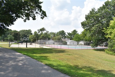 A park with a basketball court and tennis courts, surrounded by trees and grass.