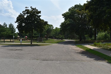 A paved path leads into a park with trees and playground equipment visible in the distance.
