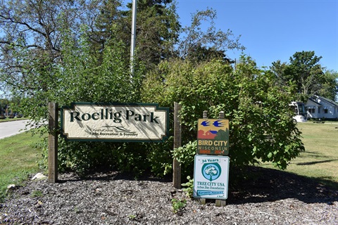 A sign for Roellig Park is shown, with smaller signs below indicating Bird City Wisconsin and Tree City USA status.