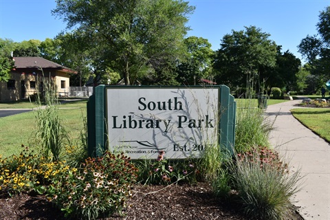 A sign for South Library Park, established in 2017, with a walking path and trees in the background.