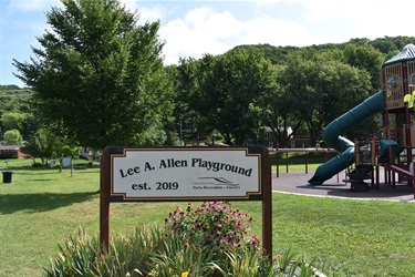 Sign for Lee A. Allen Playground established in 2019 with a playground structure in the background.