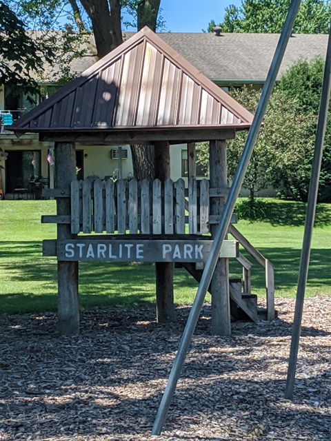 A wooden play structure with a brown metal roof and a sign that reads 