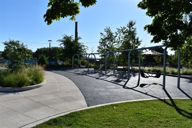 A modern playground with swings and a paved pathway on a sunny day.