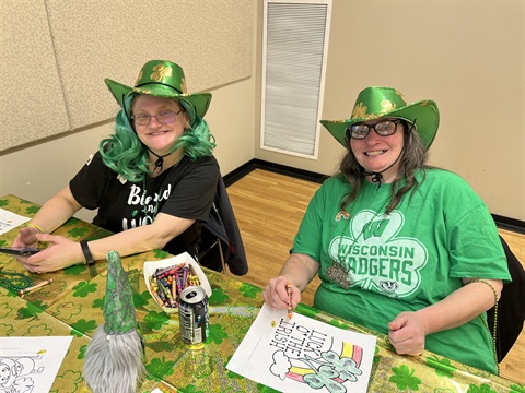2 Special Olympics athletes at a St Patrick's Day party. both wearing green and green hats. 