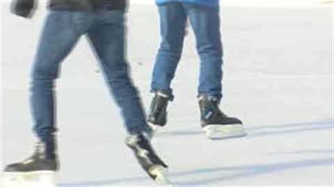 Close-up of two people ice skating on a rink, their legs and skates visible against the white ice.