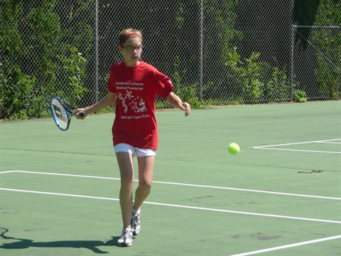 young girl playing tennis about winding up to hit tennis ball 