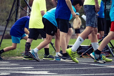 Players in bright athletic clothing and running shoes huddle and move along a track edge during a sports practice session.