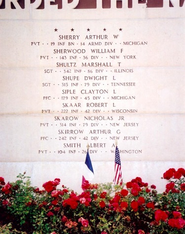 Marble grave marking listing the names of American soldiers, with red flowers and the French and American flags in front
