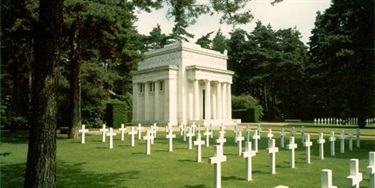 White marble cemetery mausoleum behind rows of white cross grave markers for American solders