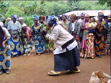Woman singing and dancing in an outdoor area surrounded by people in bright African clothing