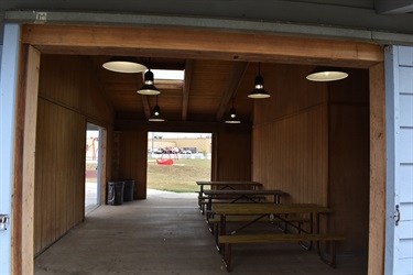 A covered picnic area with picnic tables inside and a playground visible in the distance.